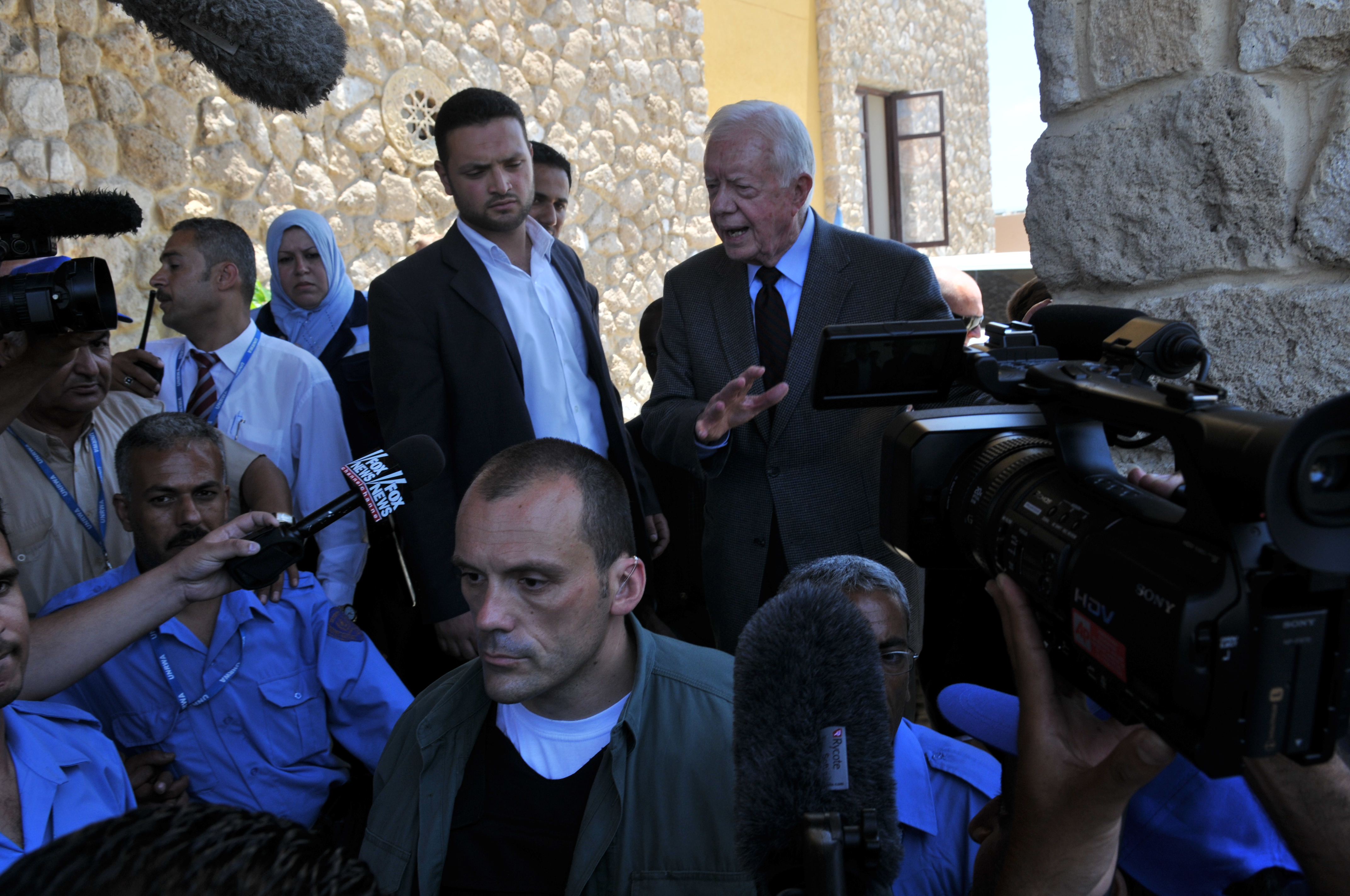 Protective personnel among reporters and cameras during a press engagement